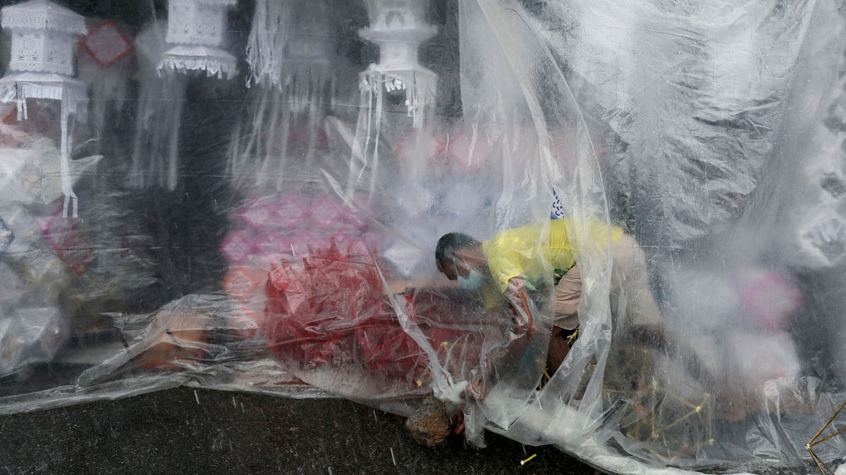 A vendor wearing a protective mask holds a cover to protect vesak lanterns he made at a roadside shop during heavy rains ahead of commemorating the birth, enlightenment and death of Buddha, amid concerns about the spread of Covid-19 in Colombo. Credit: Reuters Photo