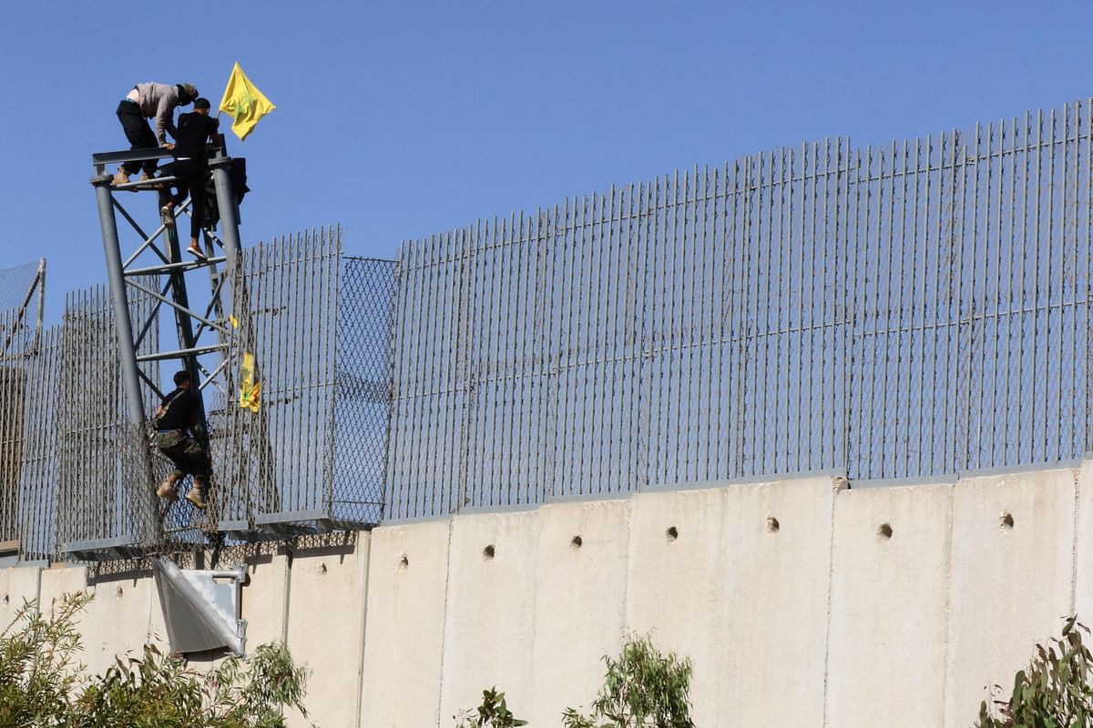Lebanese Hezbollah supporters hang the Shiite Muslim movement's yellow flat on the border fence between Lebanon and Israel on the outskirts of the southern Lebanese border village of Adaisseh, on May 25, 2021, as Lebanon marked the 21st anniversary of the Israeli withdrawal from the south of the country. Credit: AFP Photo