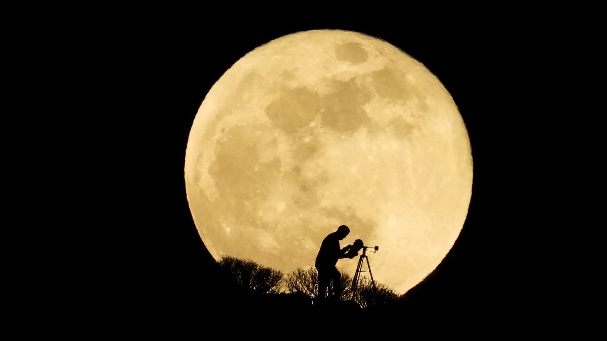A man uses a telescope to observe the full moon, known as the