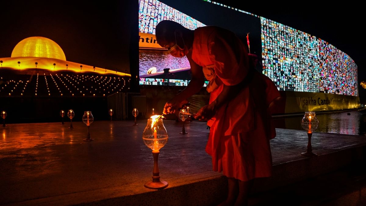 A Buddhist monk wearing a face mask lights candles as screens show devotees gathering via the Zoom application during Vesak Day, an annual celebration of Buddha's birth, enlightenment, and death at the Dhammakaya temple amid the coronavirus pandemic in Pathum Thani province, Thailand.