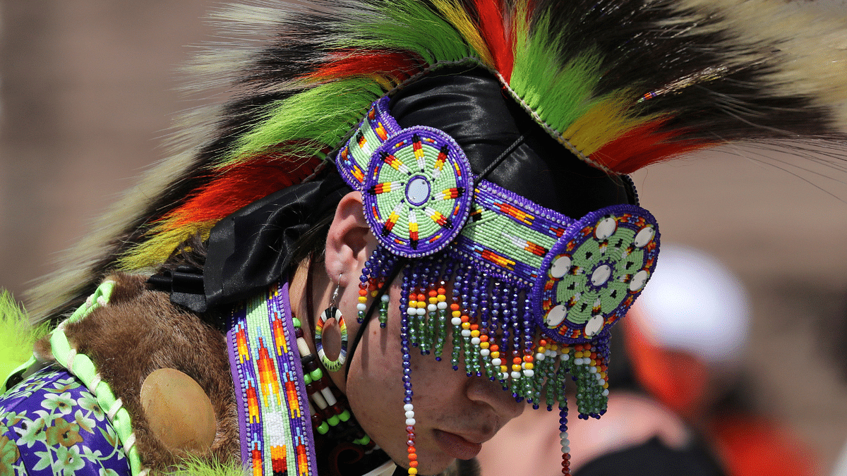 A First Nations dancer, part of a protest after the remains of 215 children were found at a residential school, prepares to march from the Ontario legislature in Toronto. Credit: Reuters Photo