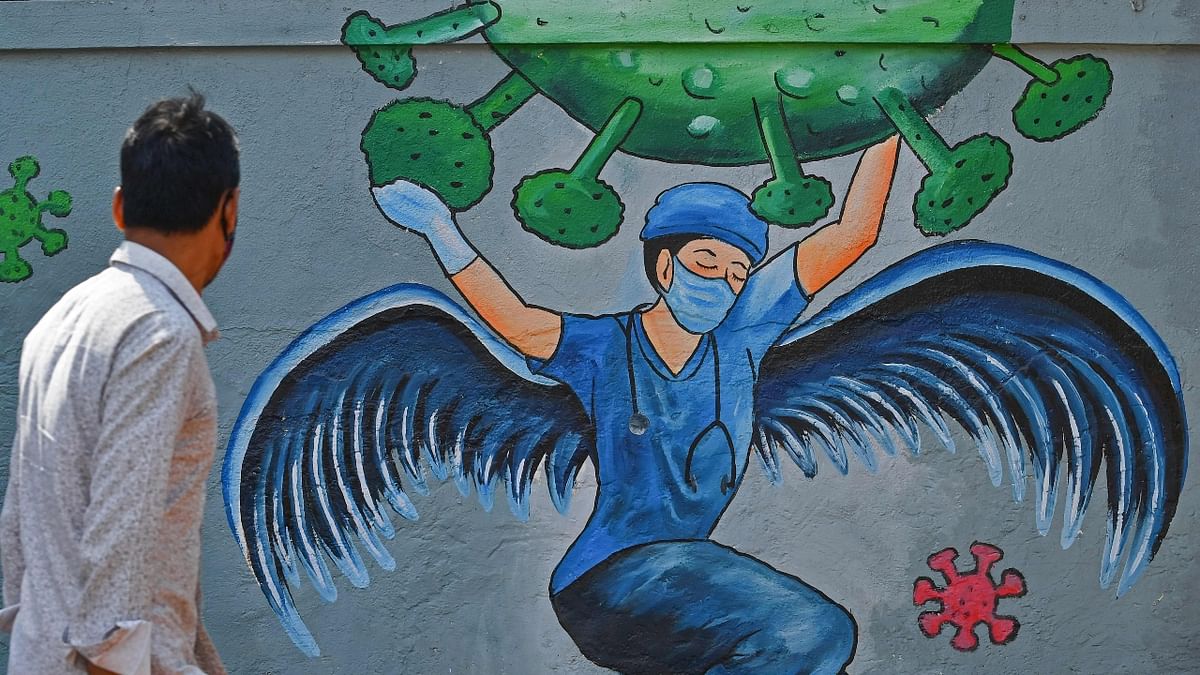 A pedestrian walks past a wall mural representing awareness measures against the Covid-19 coronavirus featuring a frontline medical staff as a guardian angel, in Navi Mumbai. Credit: AFP Photo