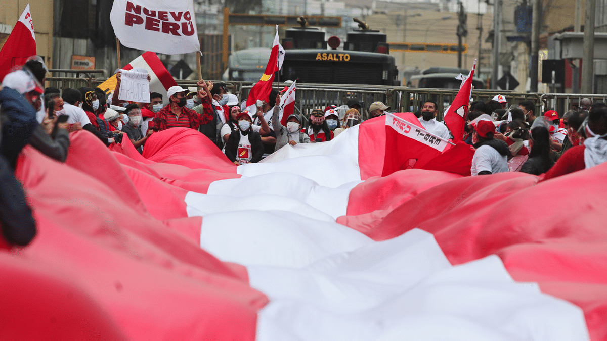 Supporters of Peru's presidential candidate Pedro Castillo hold Peru's national flag while gathering at a roadblock set up by police near the National Office of Electoral Processes, in Lima. Credit: Reuters Photo