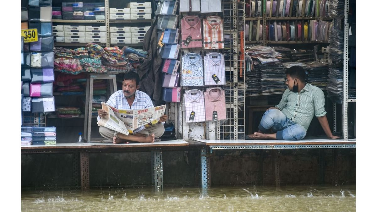 Shopkeepers sit in their shops on a waterlogged street at Hindmata in Mumbai. Credit: PTI Photo
