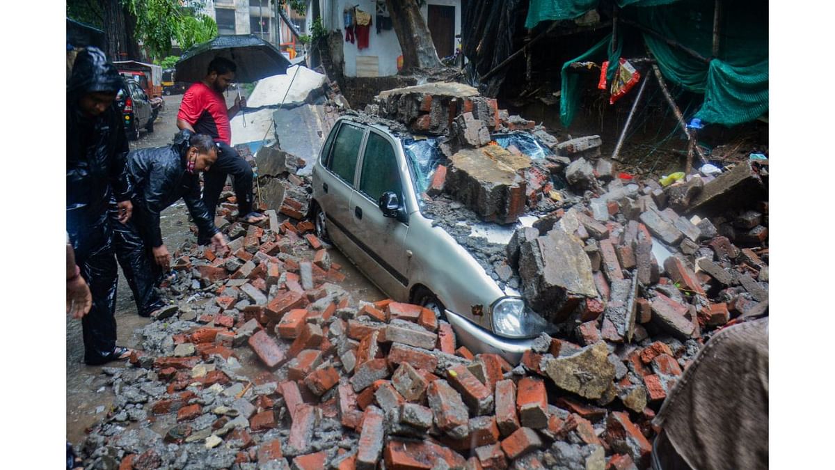 Vehicles damaged after a society compound wall fell on them following heavy rain, at Savarkar Nagar, in Thane. Credit: PTI Photo
