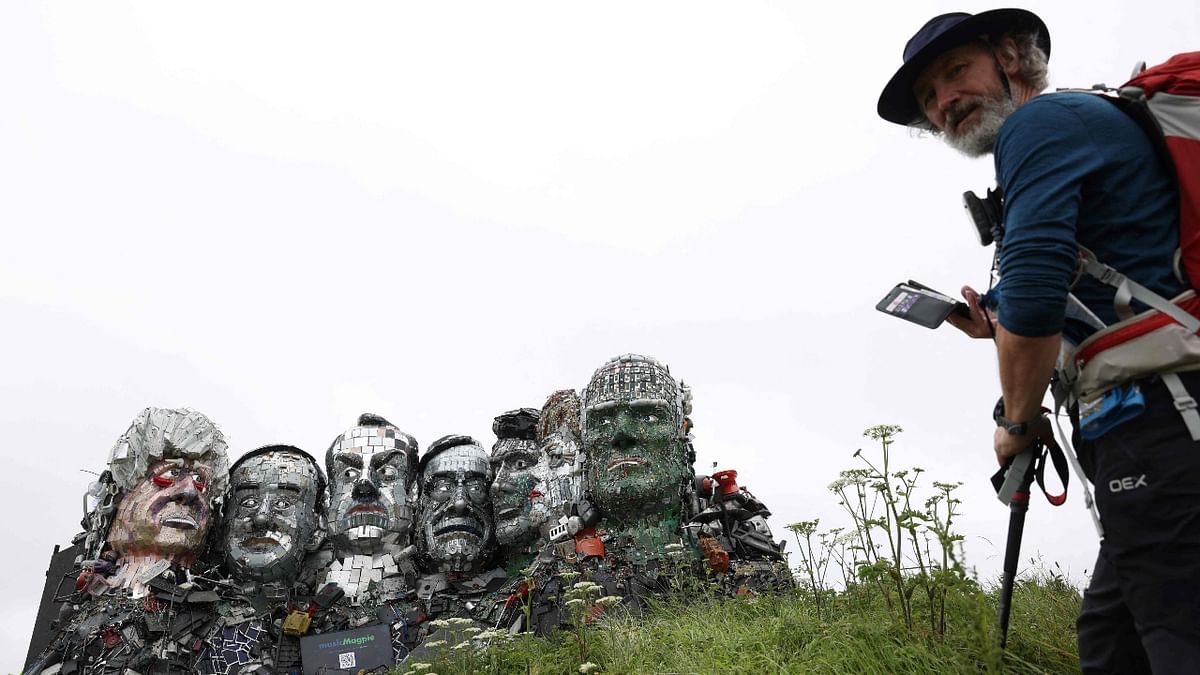 A visitor prepares to photograph a giant Mount Rushmore-style sculpture of the G7 leaders’ heads, made entirely of discarded electronics, is displayed on a beach near to Carbis Bay, Cornwall. Credit: AFP Photo