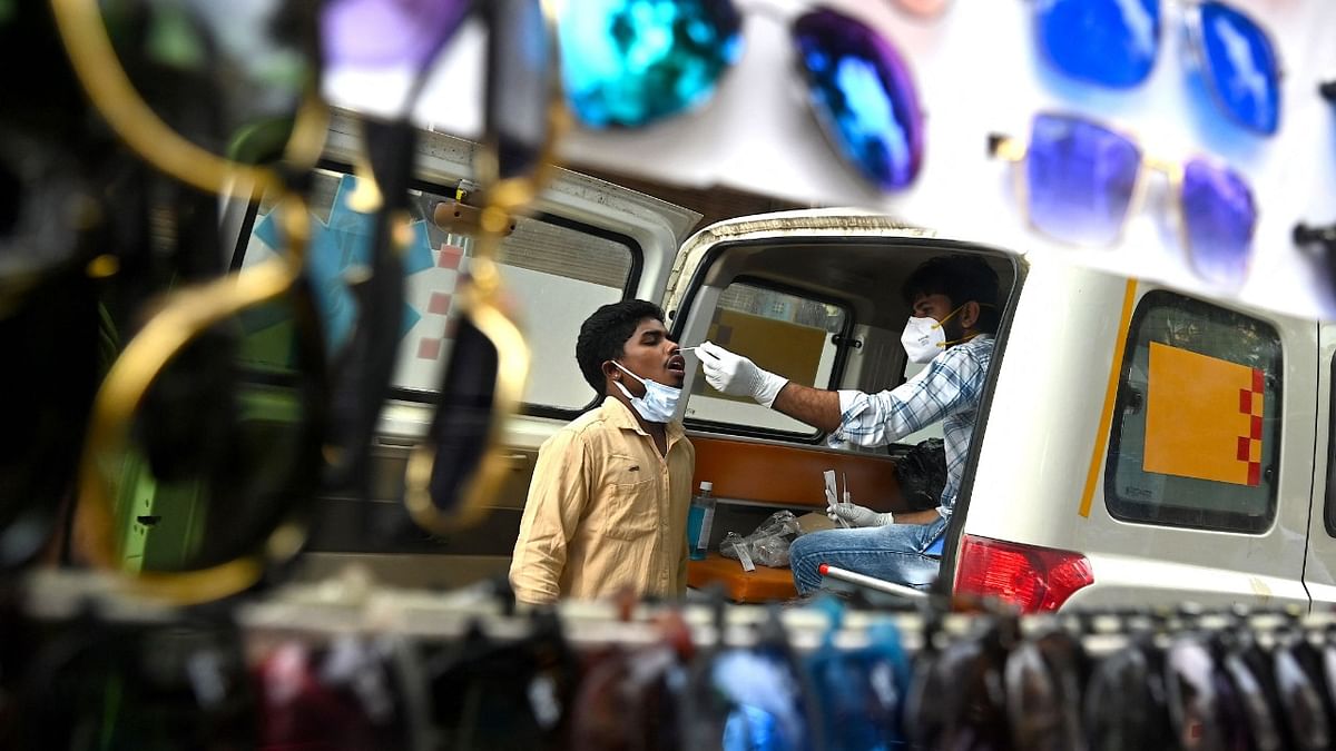 A health worker collecting a swab sample from a man to test for the Covid-19 coronavirus is seen reflected through a mirror at a roadside stall in Gurgaon. Credit: AFP Photo