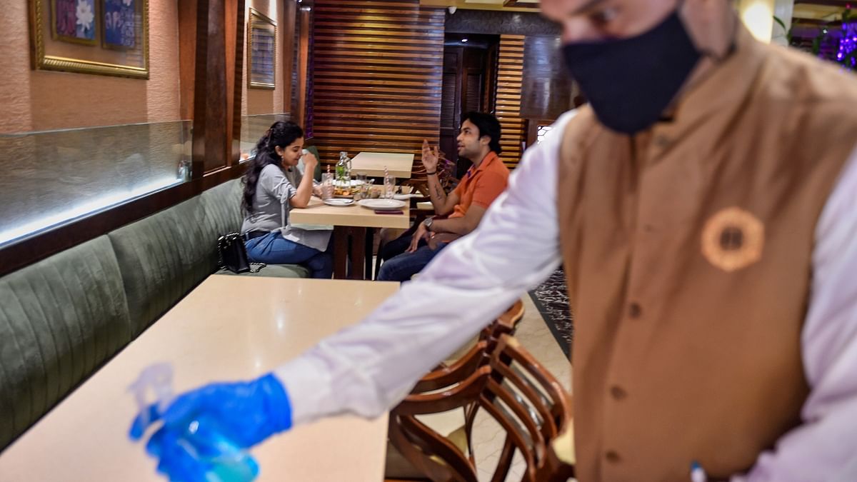 A waiter sanitises a table in a restaurant that opened after the state government eased Covid-induced restrictions, in New Delhi.