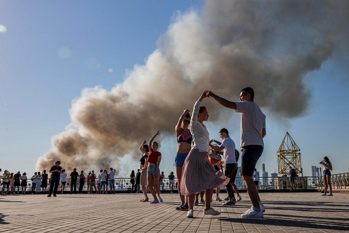 Couples dance samba as smoke rises from a burning pyrotechnics warehouse in Moscow. Credit: AFP Photo