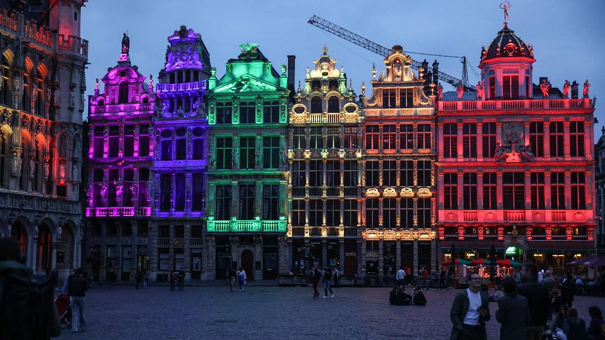 Passers-by stand next to the Brussels Town Hall and the rest of the historical Grand Place in Brussels lit with the rainbow colours to show solidarity to the LGTBQ+ community after the anti-gay vote in Hungary and the position of UEFA in Brussels. Credit: AFP Photo