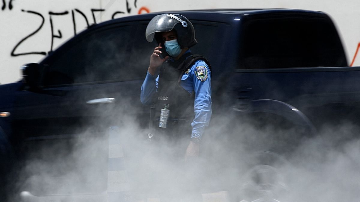 A riot police speaks on the phone amid smoke during an opposition protest against the Zones for Employment and Economic Development (ZEDES) -new type of administrative division- outside Honduras' Central Bank in Tegucigalpa. Credit: AFP Photo