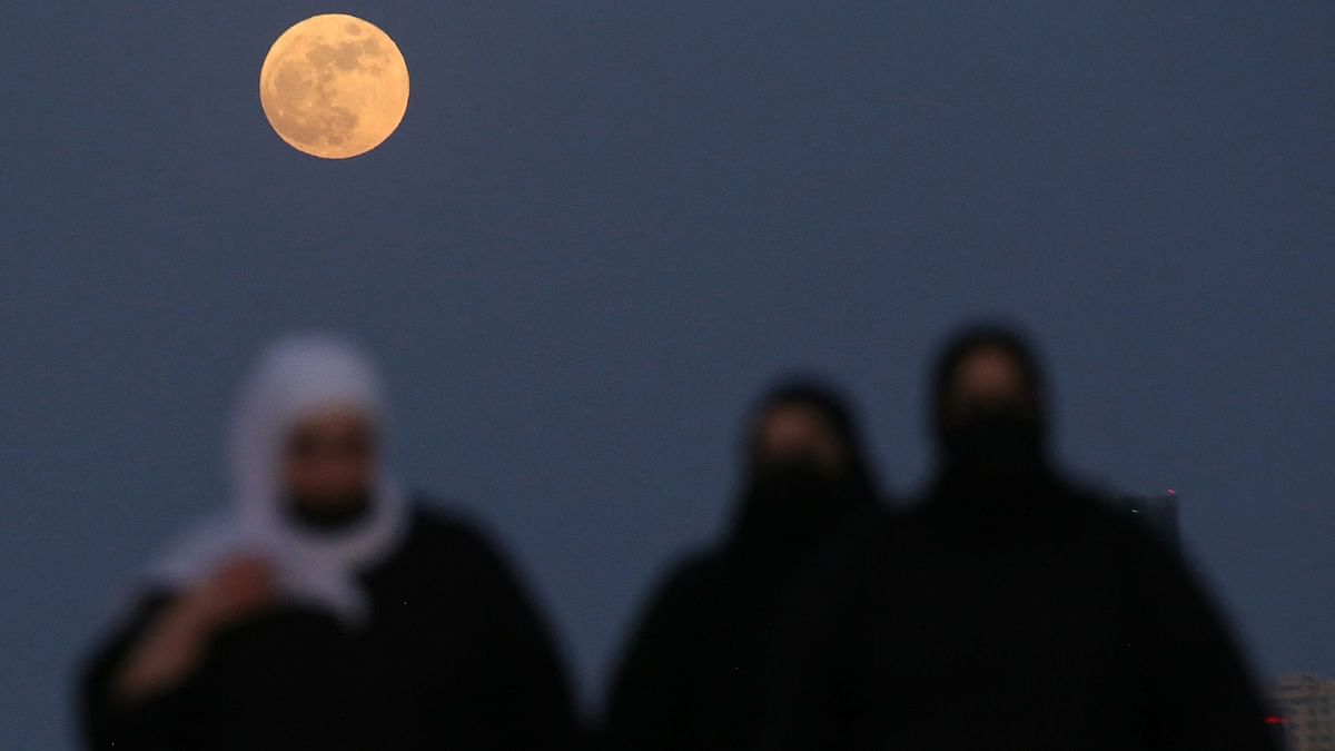 Women walk across a street as the full Strawberry Moon rises above them. Credit: AFP Photo