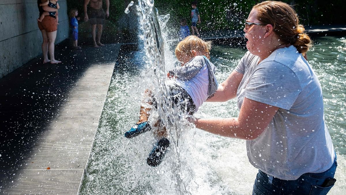 A woman holds an infant under a waterfall at a park in Washington, DC.