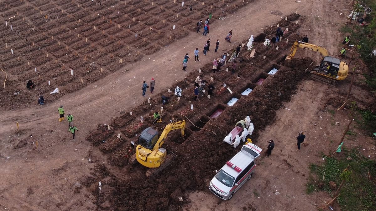 Ambulances deliver bodies to the Jakarta burial site as trucks carry away dirt beside rows of rectangles carved out of the brown earth. Credit: Reuters Photo