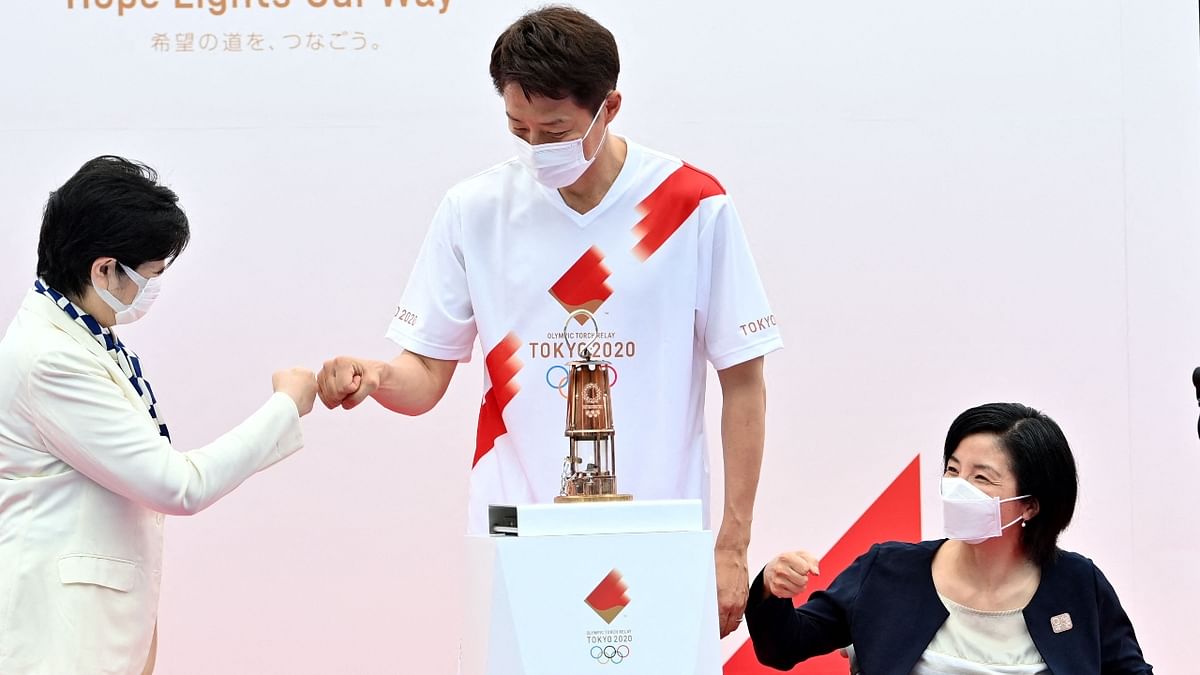 Tokyo governor Yuriko Koike fist bumps with former Japanese professional tennis player and torchbearer Shuzo Matsuoka as former Japanese Paralympian Aki Taguchi looks on during the unveiling ceremony of the Olympic flame at the Komazawa Olympic Park General Sports Ground in Tokyo. Credit: AFP Photo