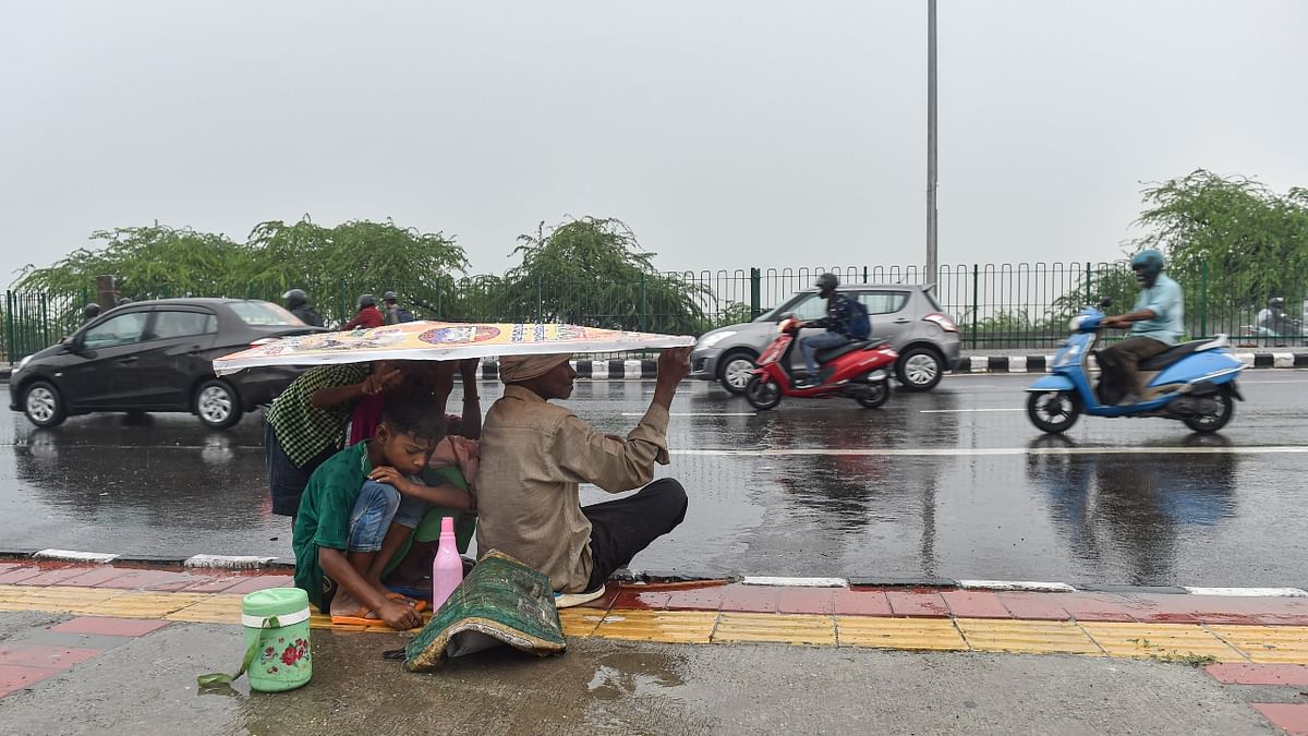 A family covers themselves under a hoarding during the rain. Credit: PTI Photo