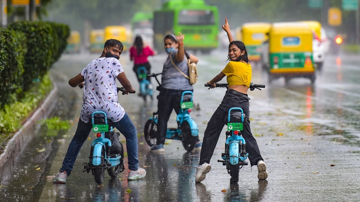 People enjoy a ride on electric bikes during rain in New Delhi.