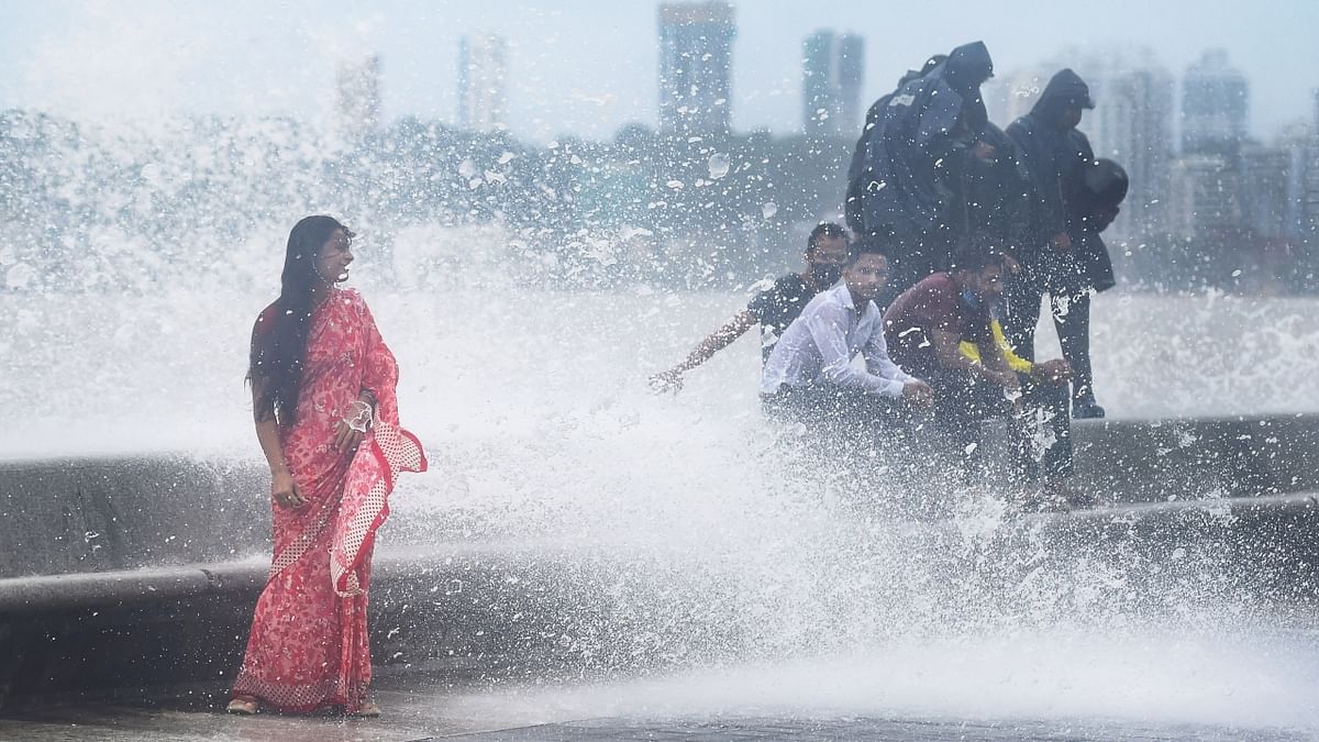 People stand amid crashing waves during high tide at Marine Drive in Mumbai. Credit: PTI Photo