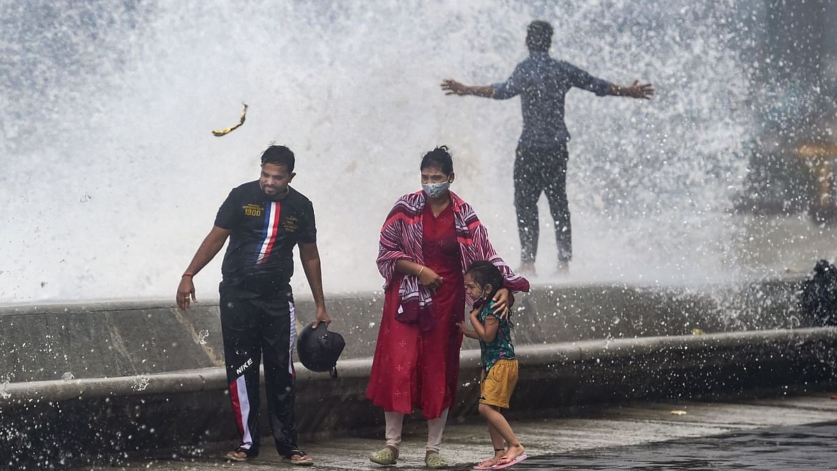 People stand amid crashing waves during high tide at Marine Drive. Credit: PTI Photo