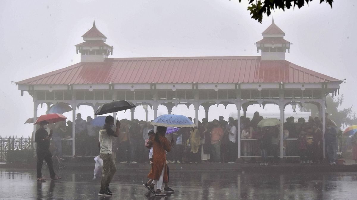 Tourists take a stroll during heavy rain at Ridge in Shimla. Credit: PTI Photo