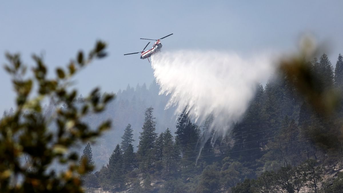 A CH helicopter siphons water from the North Fork of the Feather River near Pulga, CA and drops on the mountainside as the Dixie Fire grows in Plumas National Forest, California. Credit: Reuters Photo