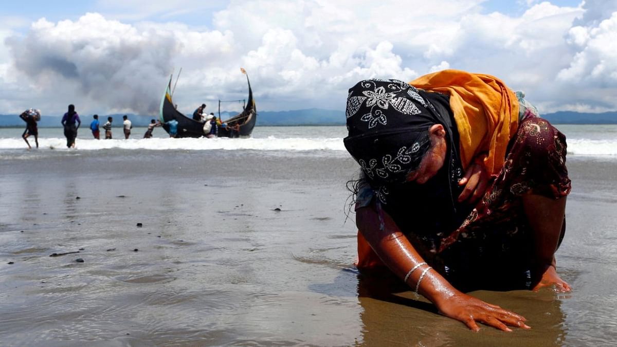 An exhausted Rohingya refugee woman touches the shore after crossing the Bangladesh-Myanmar border by boat through the Bay of Bengal in Shah Porir Dwip. (Credit: Reuters Photos/Danish Siddiqui)