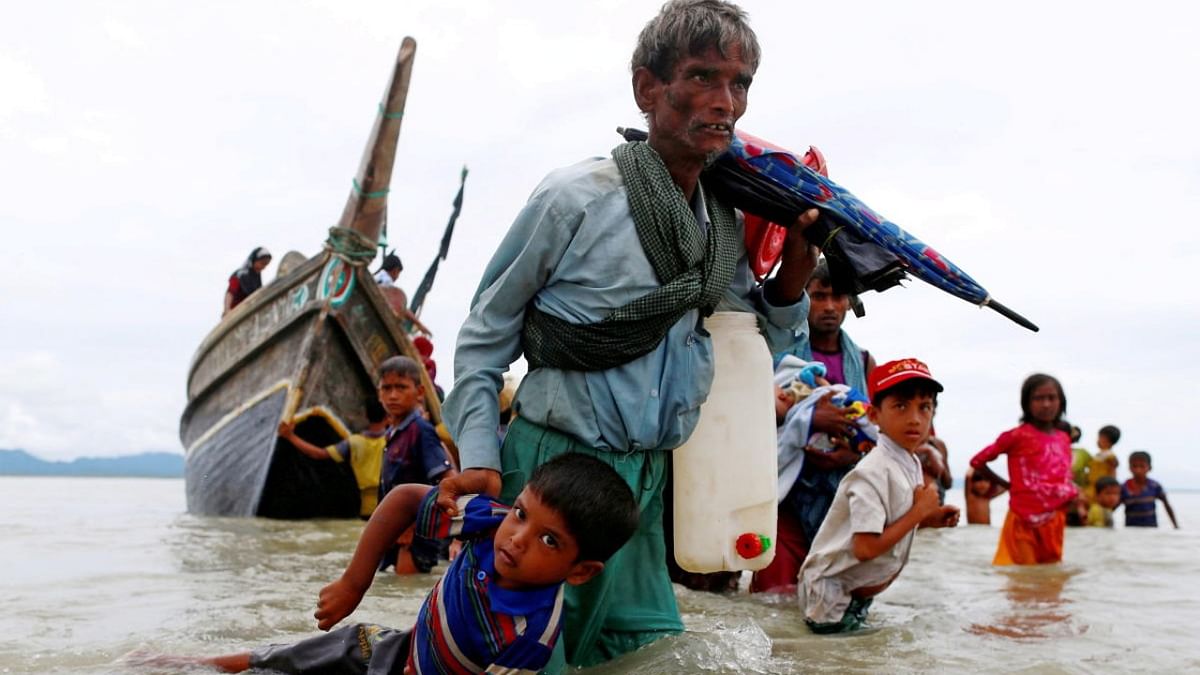 A Rohingya refugee man pulls a child as they walk to the shore after crossing the Bangladesh-Myanmar border by boat through the Bay of Bengal in Shah Porir Dwip. (Credit: Reuters Photos/Danish Siddiqui)
