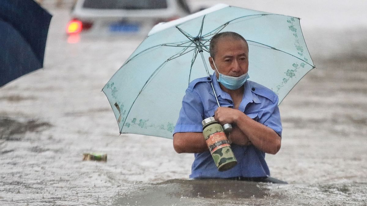 The picture shows a man wading through flood waters along a street following heavy rains in Zhengzhou in Henan province. Credit: AFP Photo