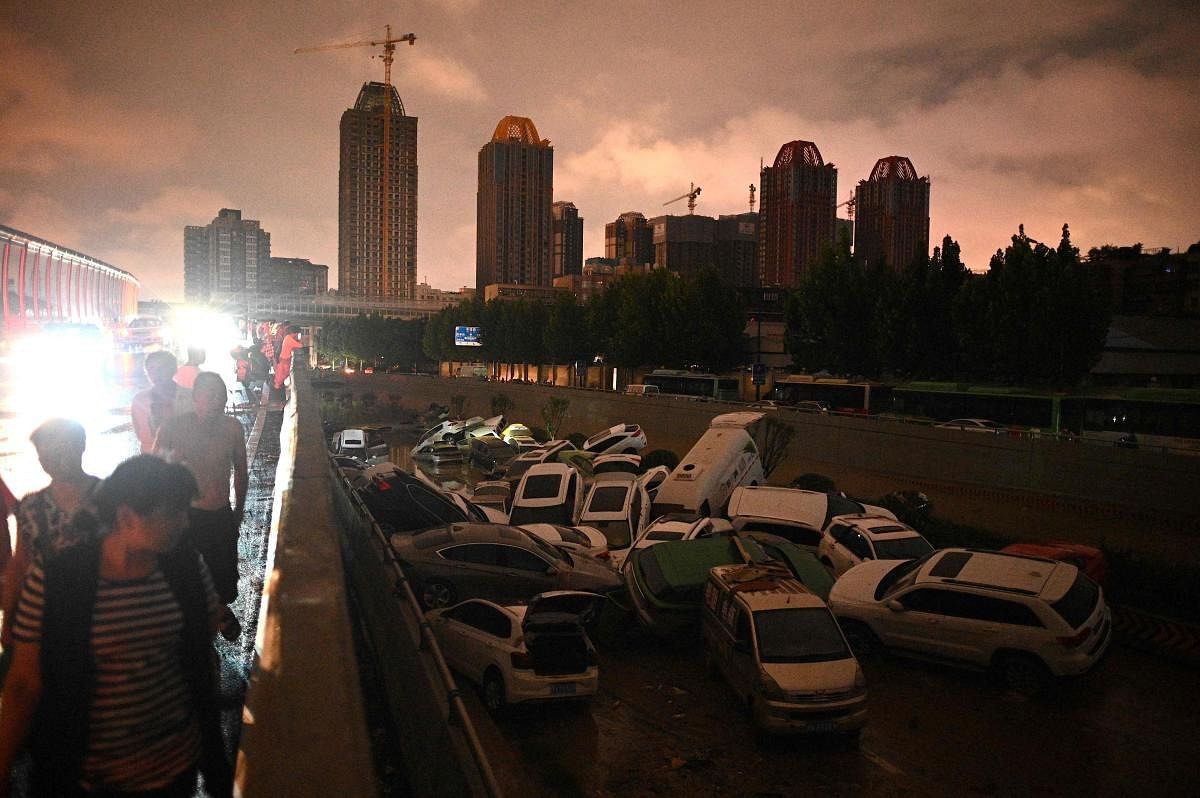 People look at cars stacked on each other at an entrance of a tunnel following a heavy rain in Zhengzhou in China's Henan province. Credit: AFP Photo