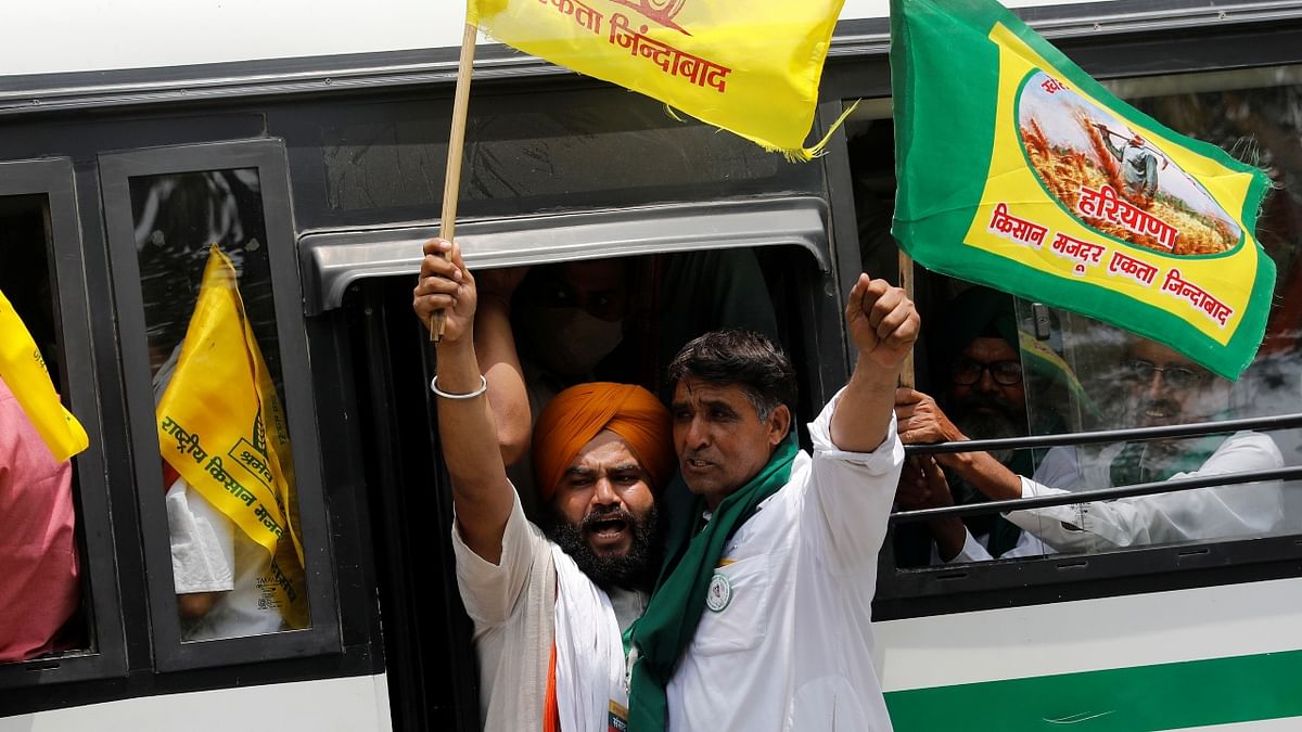 Farmers wave flags as they arrive in a bus to attend a sit-in protest against the farm laws, near parliament house, in New Delhi. Credit: Reuters Photo