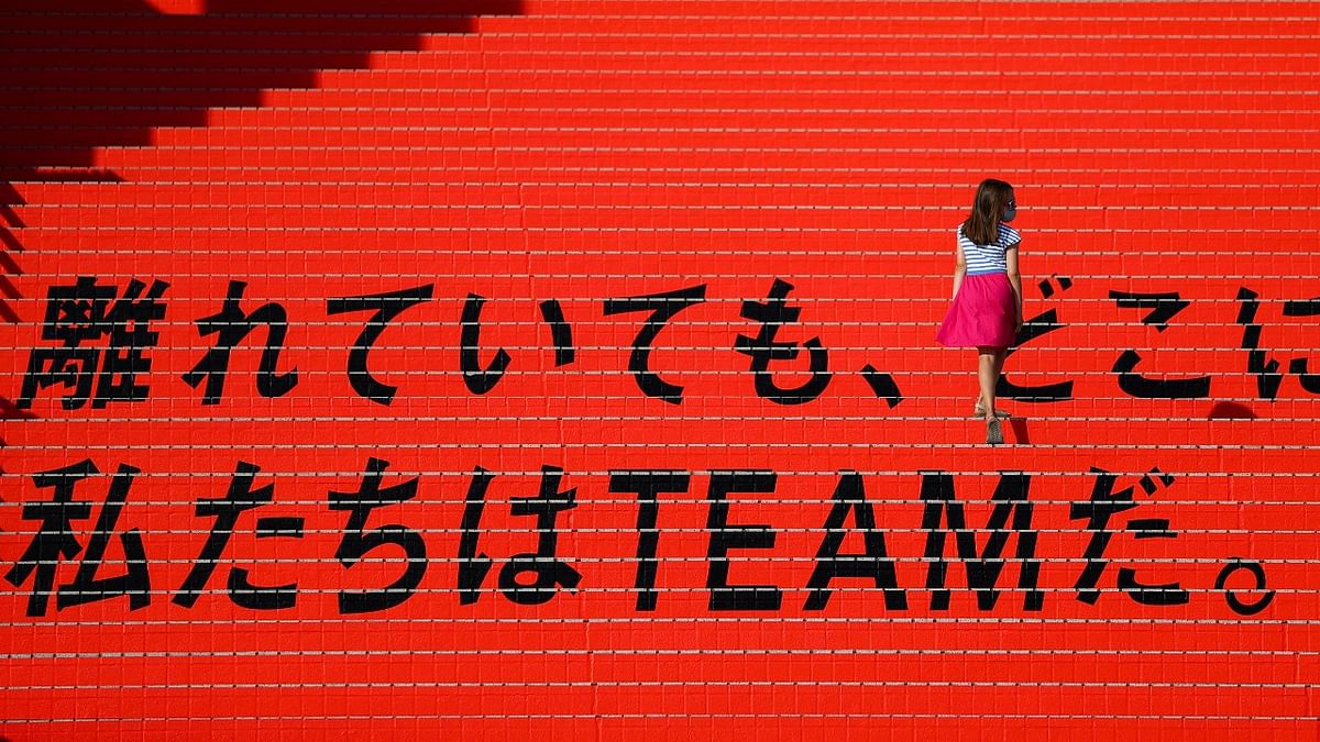 A woman wearing a protective face mask walks on an Olympics decoration with a message reading