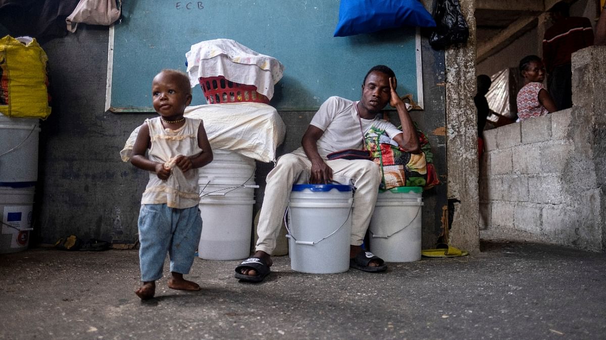 A man sleeps on top of buckets as a child looks on at a school where people with disabilities and their families have been taking shelter after their settlement was burned down by gangs a month ago, in Port-au-Prince. Credit: Reuters photo