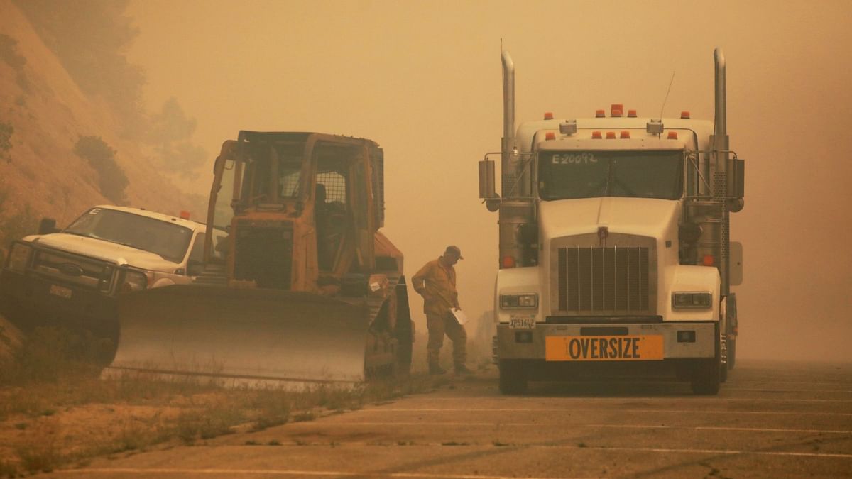 A person walks next to vehicles amongst the smoke from the Dixie Fire along Bucks Lake Road, Meadow Valley, California