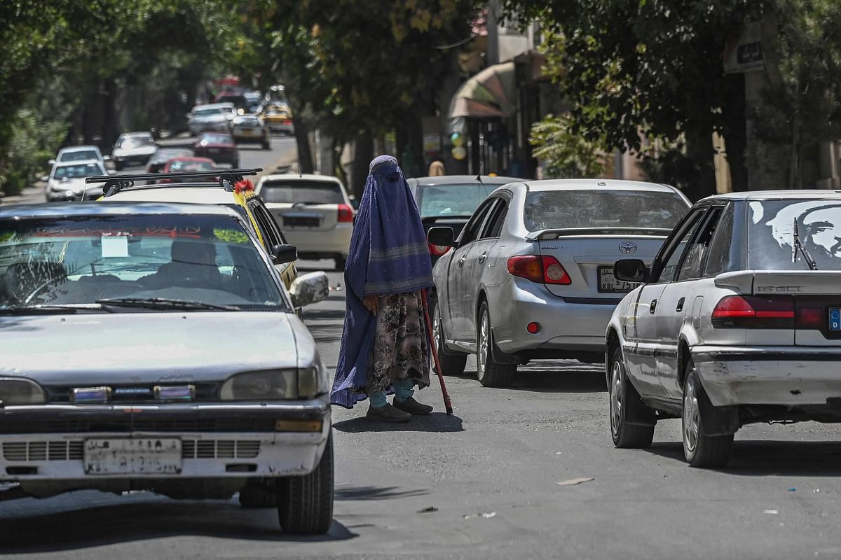 A burqa clad woman seeks alms from the commuters as she stands in the middle of a road in Kabul. Credit: AFP Photo