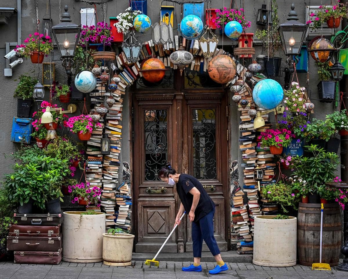 A woman sweeps the pavement the entrance of a cafe decorated with vintage items in Moscow. Credit: AFP Photo