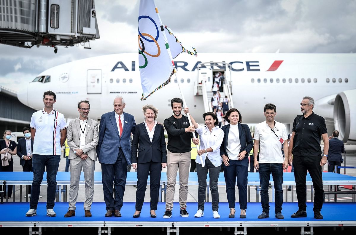 Authorities pose for a group photograph with the Olympic flag marking the handover from Japan to the next Games in Paris 2024, as French athletes return from the Tokyo Olympic 2020 games at Roissy-Charles de Gaulle airport, north of Paris. Credit: AFP Photo