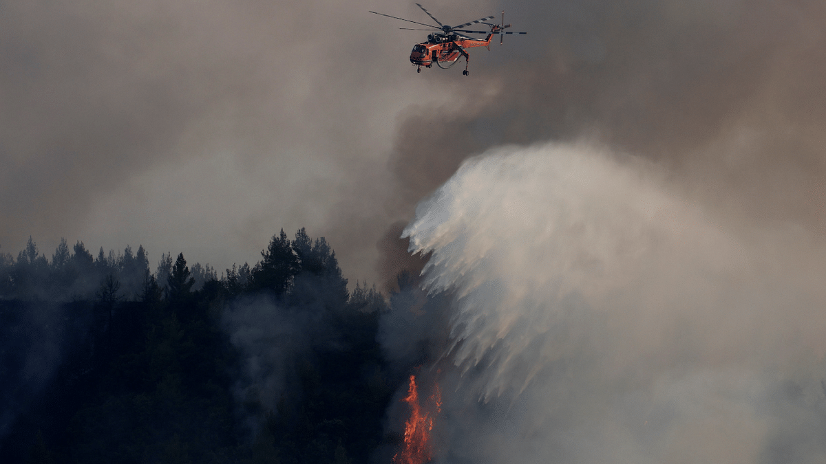 A firefighting helicopter makes a water drop as a wildfire burns in the village of Galatsona, on the island of Evia, Greece. Credit: Reuters Photo