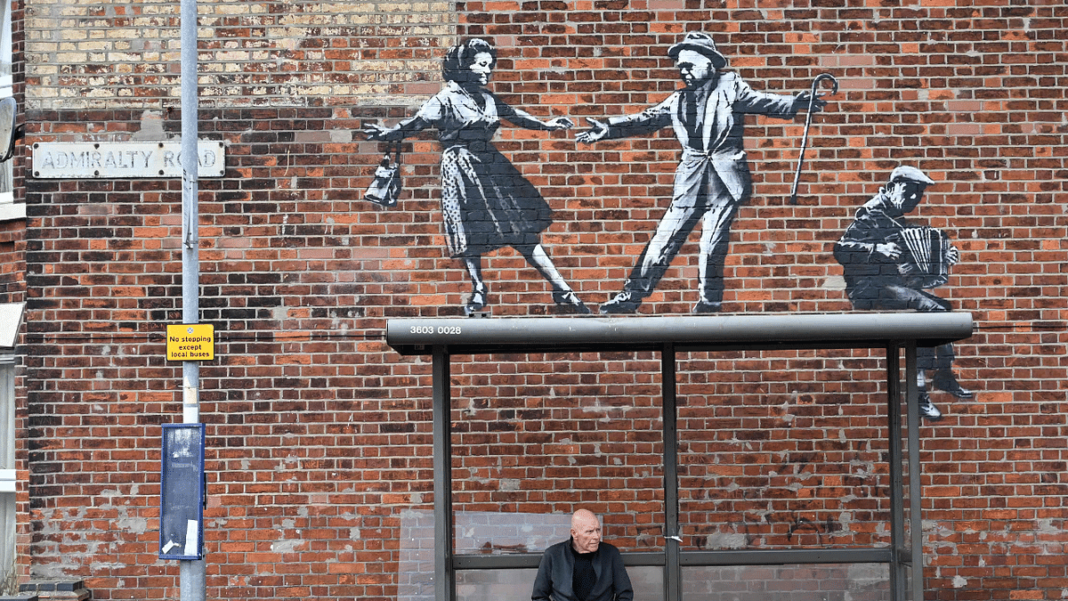 A man waits at a bus stop below a graffiti artwork of a couple dancing to an accordion player, which bears the hallmarks of street artist Banksy, on a wall in Great Yarmouth on the East coast of England. Credit: AFP Photo