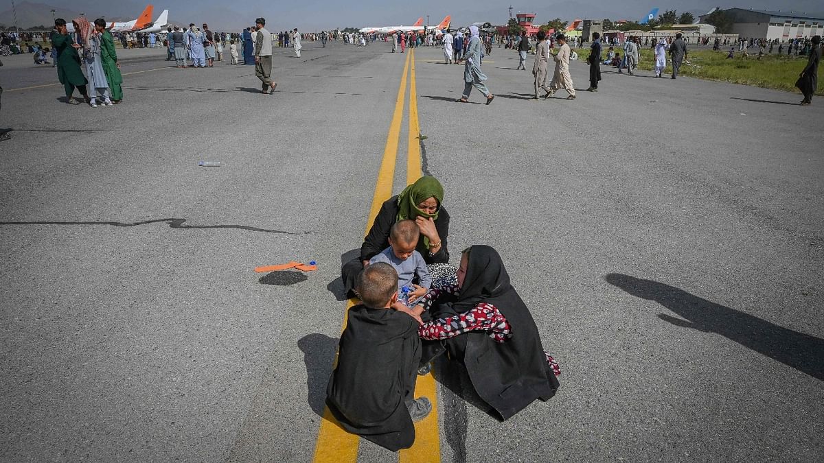 Afghan people sit along the tarmac as they wait to leave the Kabul airport in Kabul. Credit: AFP Photo