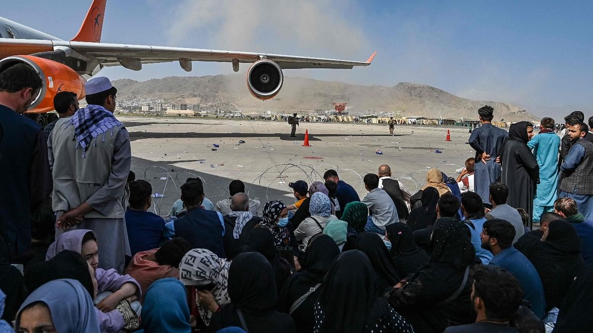 Afghan people sit as they wait to leave the Kabul airport. Credit: AFP Photo