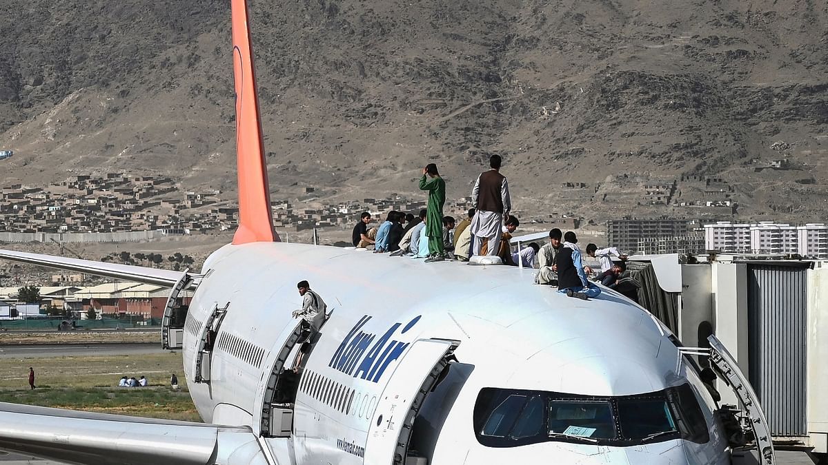 Afghan people climb atop a plane as they wait at the Kabul airport in Kabul on August 16, 2021. Credit: AFP Photo