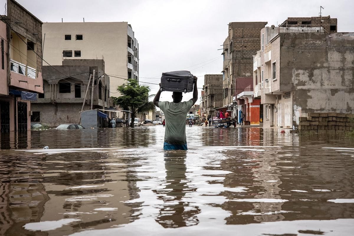 A man carries a suitcase as he moves his belongings out of his house in the flooded neighbourhood of Keur Massar, Dakar. Credit: AFP Photo
