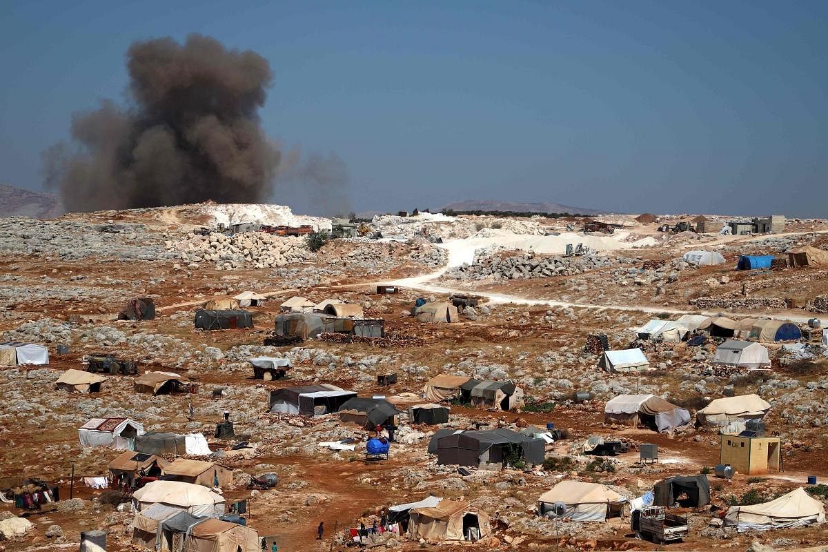 A plume of smoke rises behind a hill, where internally displaced Syrians have set tents, during reported airstrikes by pro-regime forces, north of the rebel-held city of Idlib. Credit: AFP Photo