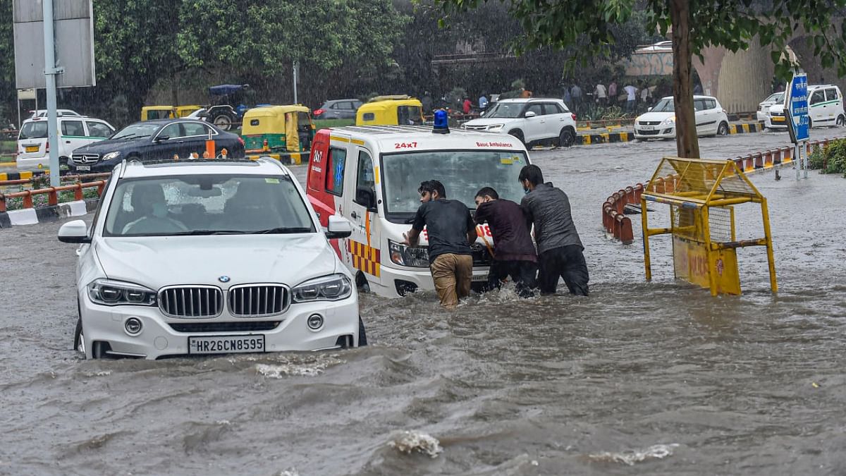 The heavy burst of rain submerged several areas, including the diplomatic enclave of Chanakyapuri, in knee-deep water and affected traffic movement in parts of the city. People try to push an ambulance as it stopped working due to a waterlogged road after heavy rain near AIIMS Hospital in New Delhi. Credit: PTI Photo