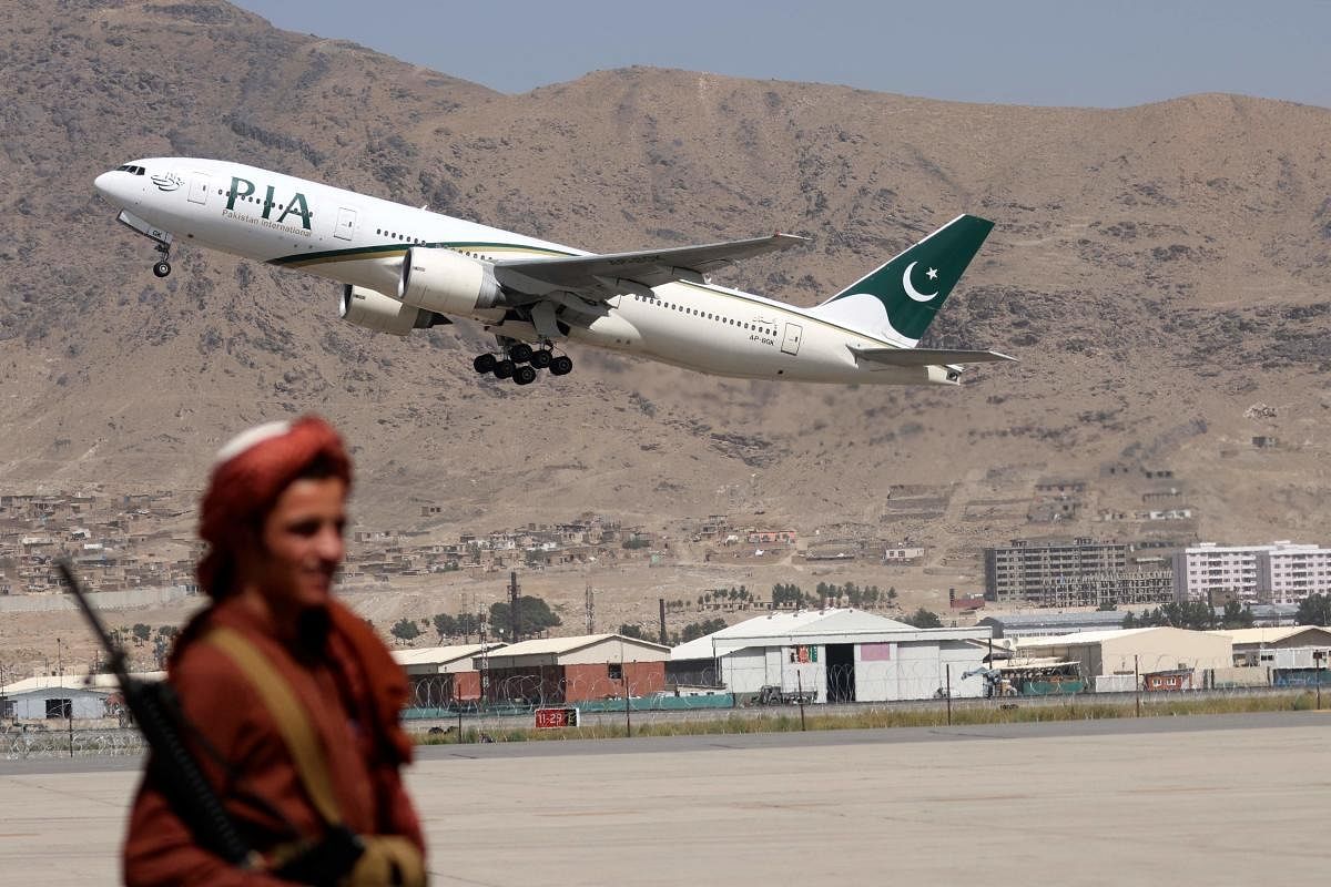 A Taliban fighter stands guard as a Pakistan International Airlines plane, the first commercial international flight to land since the Taliban retook power last month, takes off with passengers onboard at the airport in Kabul. Credit: AFP Photo