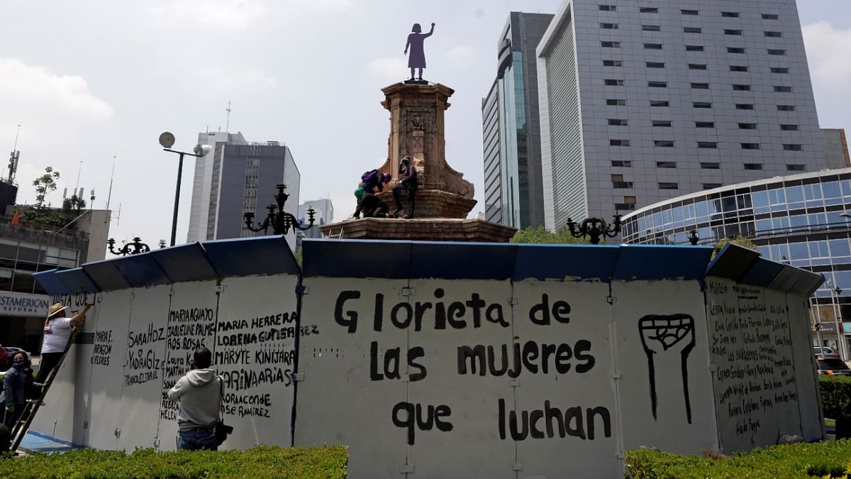 Women paint the fence protecting the site where the statue of Christopher Columbus once stood, after activists unveiled an anti-monument dedicated to