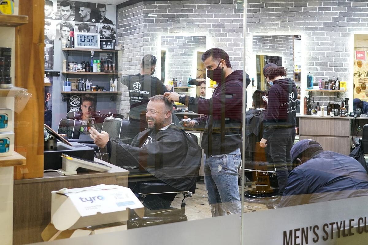 Customers receive haircuts at a city centre barber shop on the first day of many such businesses re-opening to vaccinated patrons, following months of lockdown orders that closed businesses to curb an outbreak of the coronavirus disease (COVID-19), in Sydney, Australia. Credit: Reuters Photo
