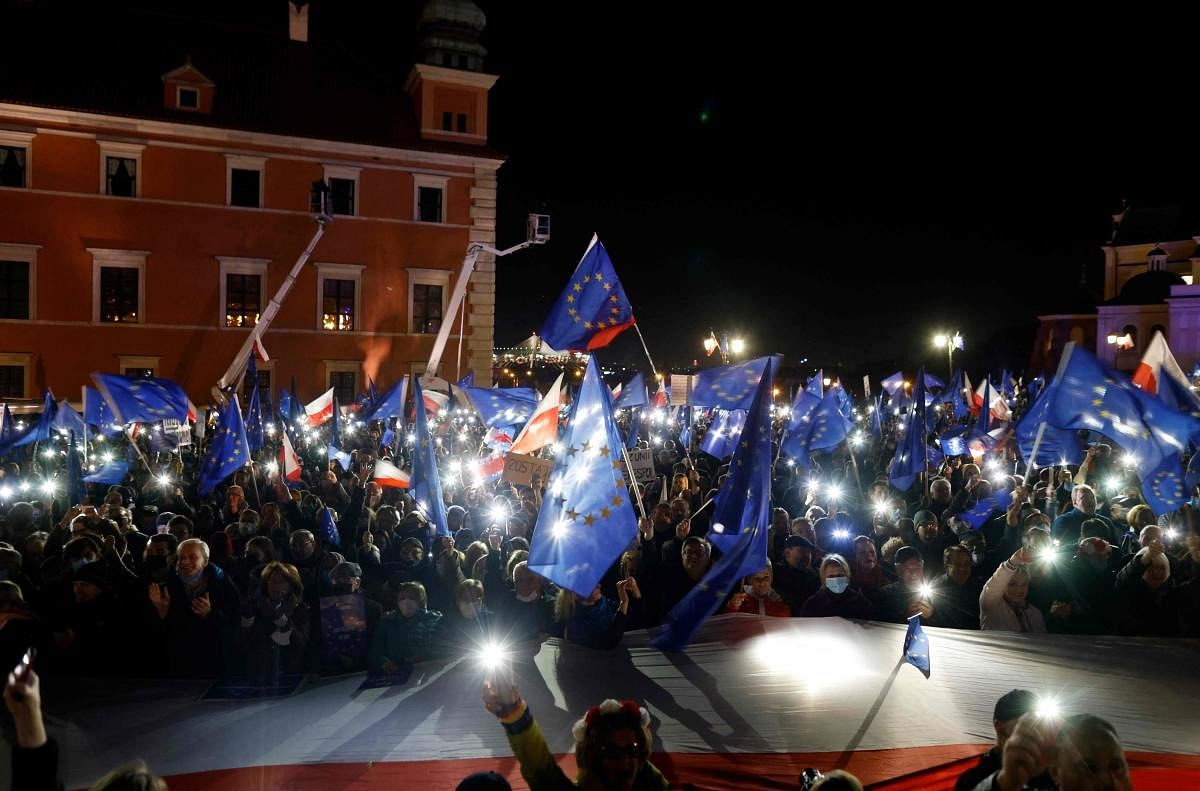 Participants show the light of their mobile phones and wave EU flags over a large Polish flag as they take part in a pro-EU demonstration following a ruling of the Constitutional Court against the primacy of EU law in Poland, in front of the Royal Castle at the central square in Warsaw. Credit: AFP Photo