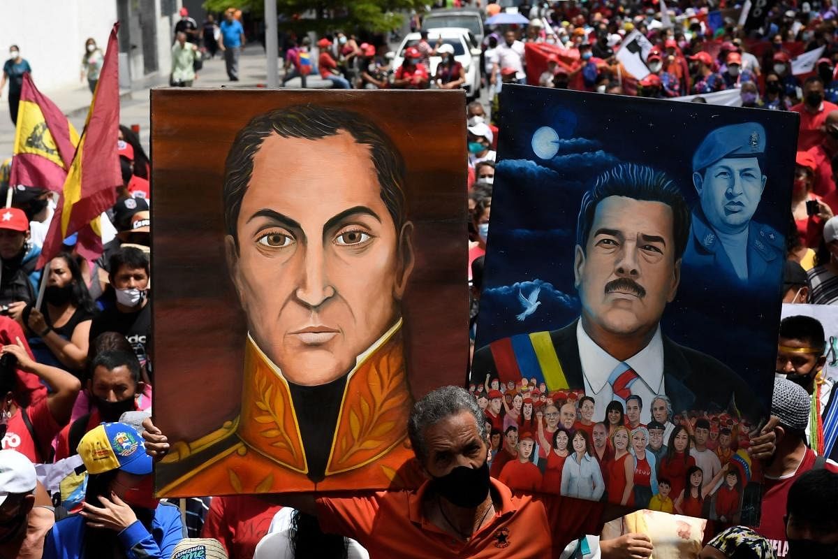 A supporter of Venezuela's President Nicolas Maduro, holds portraits of him (R) and Venezuela's national heroe Simon Bolivar, during a march to commemorate the day of Indigenous Resistance, in Caracas. Credit: AFP Photo