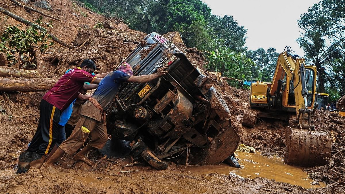 Rescue workers push a overturned vehicle stuck in the mud and debris at a site of a landslide claimed to be caused by heavy rains in Kokkayar, Kerala. Credit: AFP Photo
